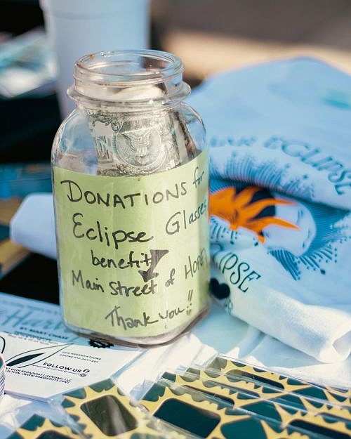Donation jar benefiting Main Street of Hope among the eclipse swag of t-shirts and buttons for sale alongside free eclipse glasses offered to commemorate the Total Eclipse of the Hope on the Hope Town Square April 8, 2024. Photo credit: Main Street of Hope.
