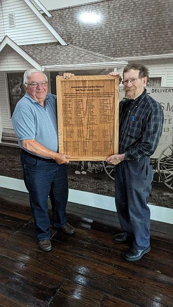 Ed Johnson (left) and John Ziegler (right) hold the plaque engraved with the list of names of those who have donated to fund the Rural Letter Carriers Museum. Photo credit: Kim Ray.